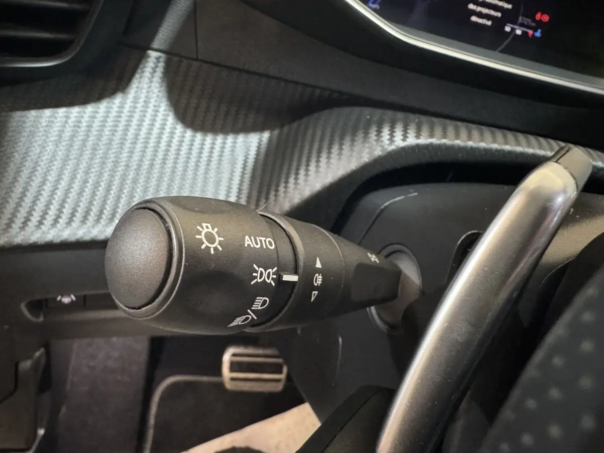 Gros plan sur la commande d’éclairage noire avec réglage automatique dans l’habitacle d’une Peugeot 208 gris clair.