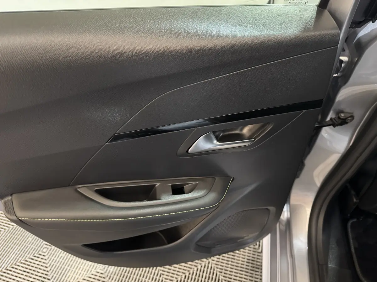 Vue intérieure de la porte arrière droite gris clair de la Peugeot 208 Hybrid 136 eDCS6 GT avec poignée argentée et surpiqûres vertes.