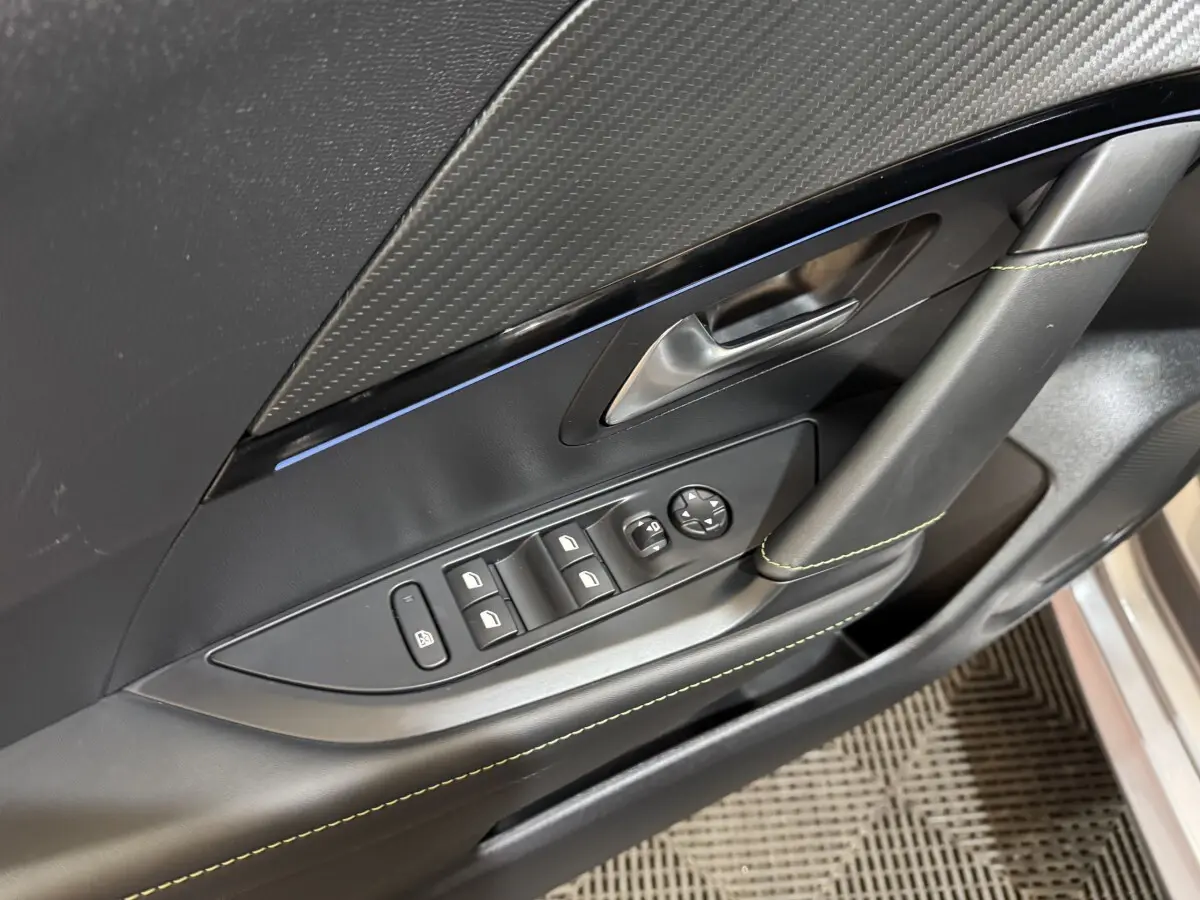 Détail de la porte côté conducteur de la Peugeot 208 Hybrid gris clair, avec commandes électriques et surpiqûres vertes.