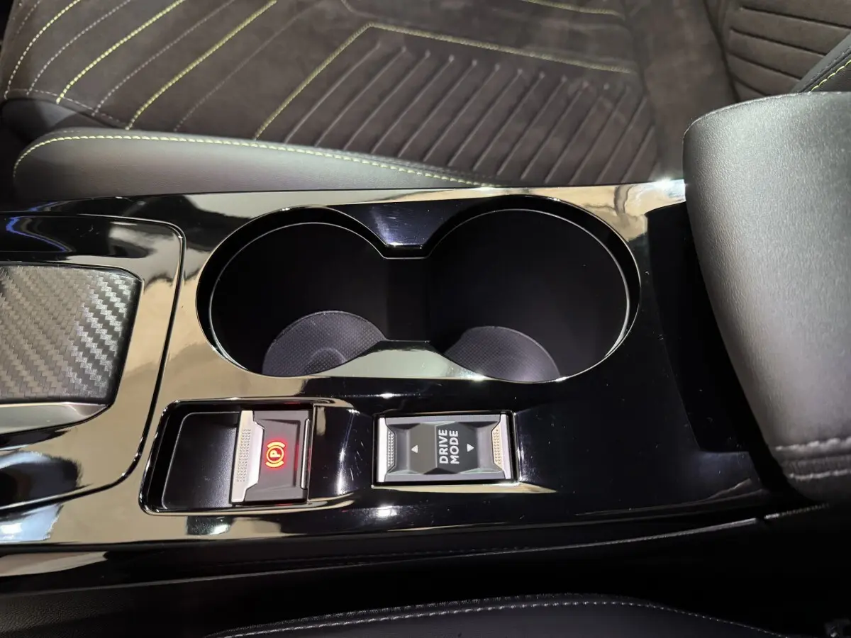 Gros plan sur la console centrale noire brillante de la Peugeot 208 Hybrid 136 eDCS6 GT avec porte-gobelets et commandes électriques.