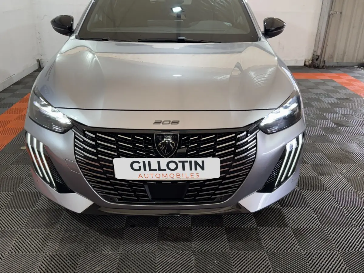 Vue avant frontale d'une Peugeot 208 Hybrid 136 eDCS6 GT gris clair avec calandre noire et feux LED allumés.