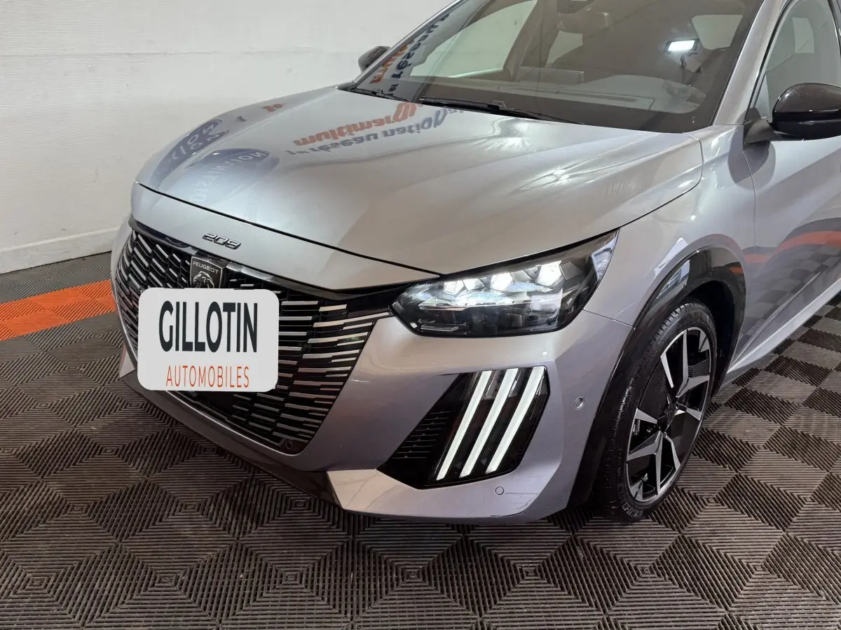 Vue 3/4 avant droit d'une Peugeot 208 Hybrid gris clair avec phares LED et signature lumineuse verticale distinctive.
