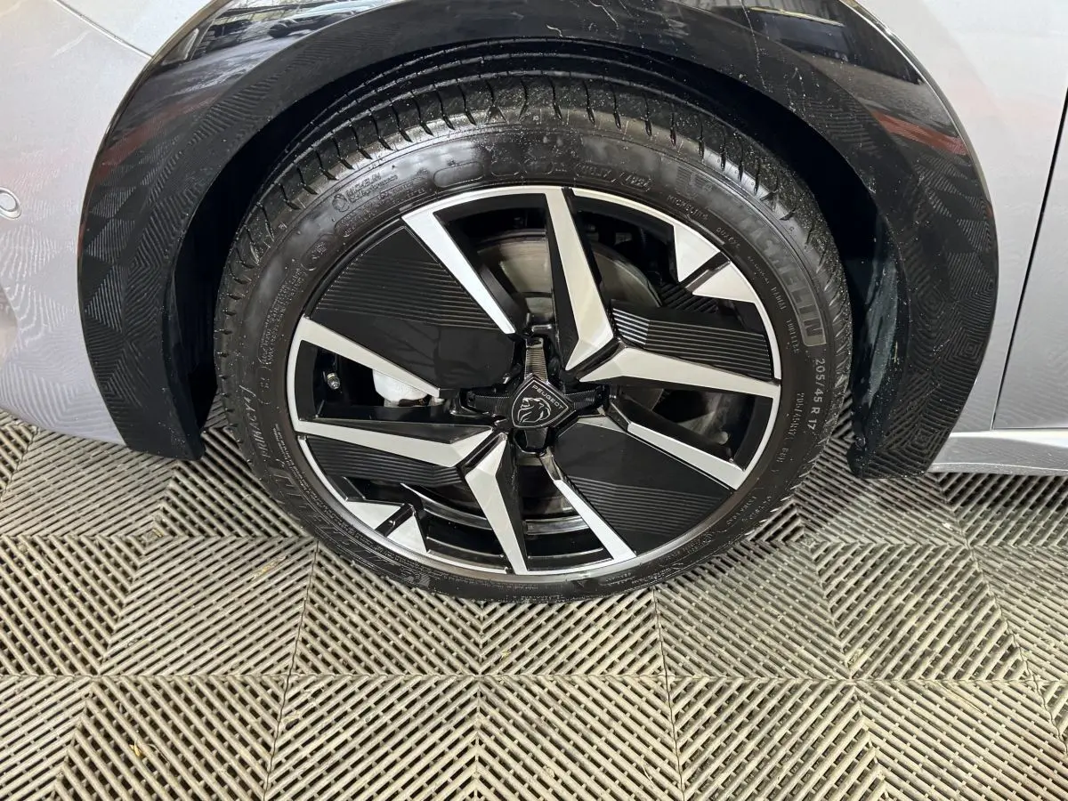 Gros plan sur la roue avant gauche de la Peugeot 208 Hybrid 136 eDCS6 GT gris clair avec jante alliage noire et argent.