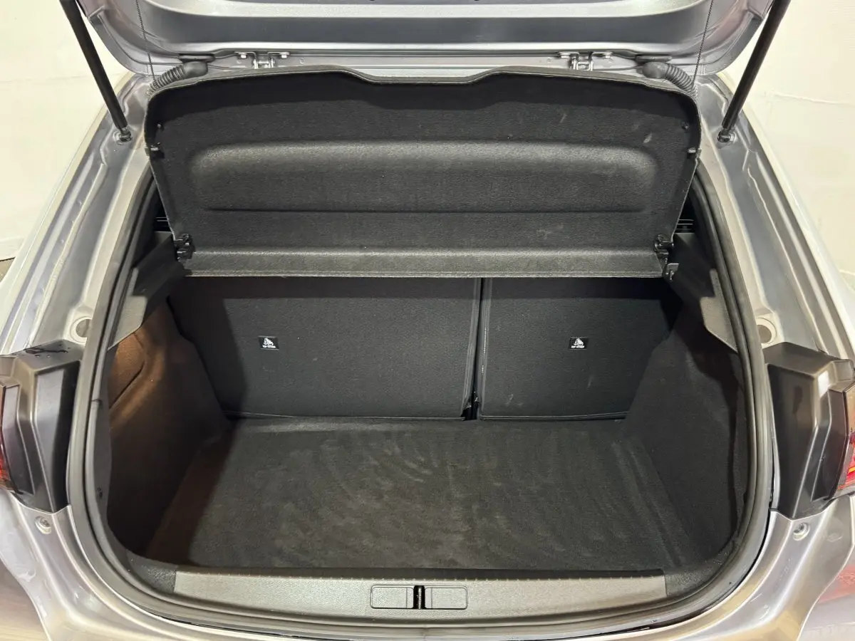 Coffre ouvert vu de l'arrière d'une Peugeot 208 Hybrid 136 eDCS6 GT gris clair, espace de chargement vide et propre.