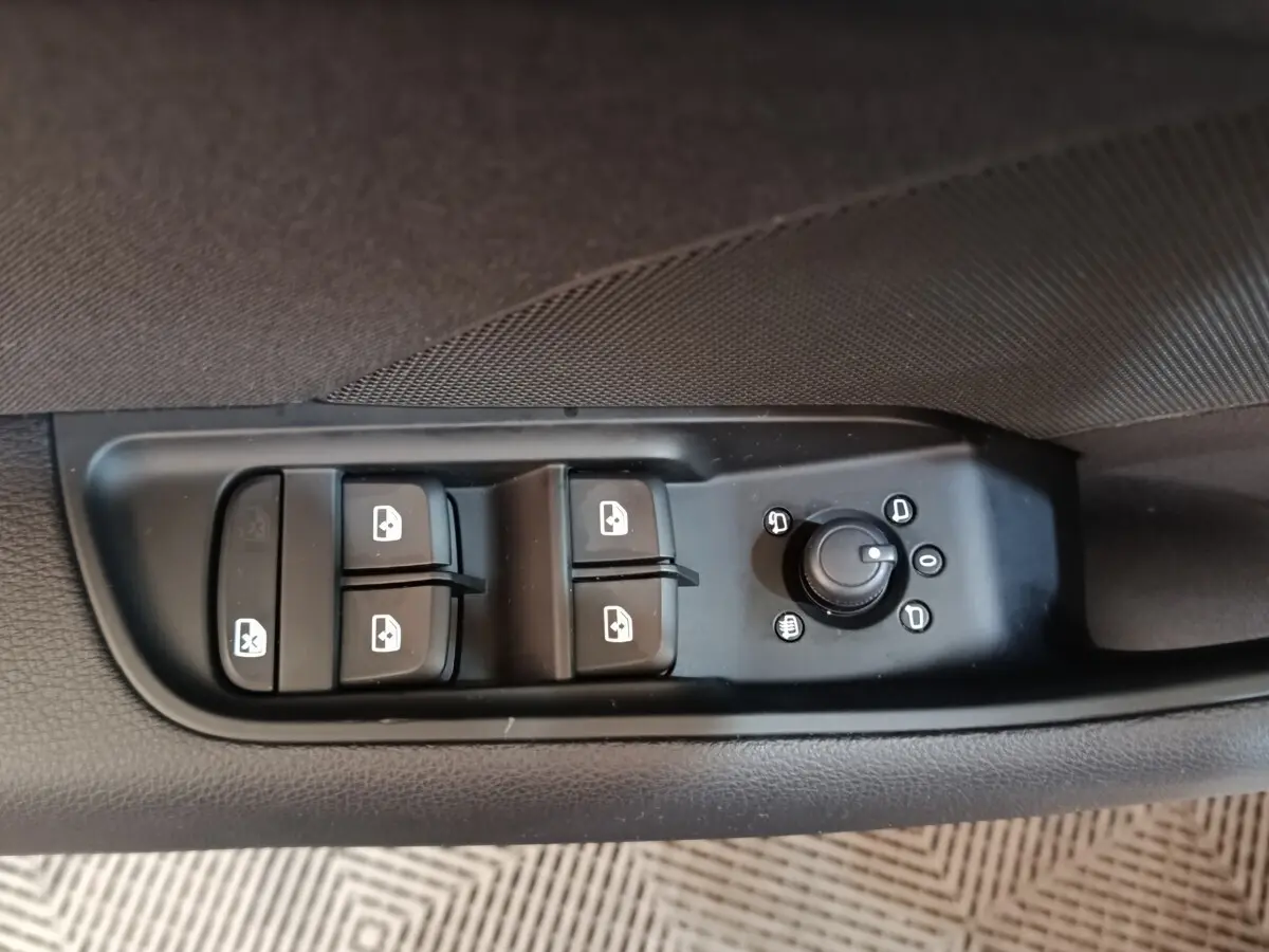 Gros plan sur les commandes de lève-vitres et réglage des rétroviseurs côté conducteur d'une Audi A3 blanche.