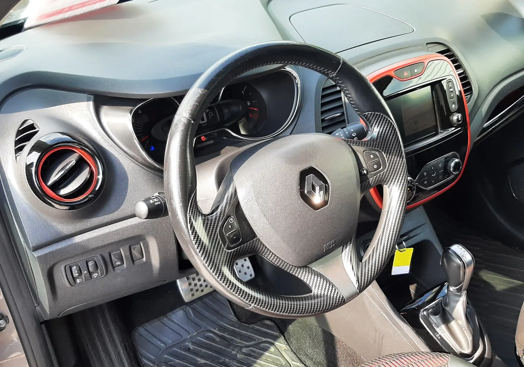 Vue intérieure du volant et tableau de bord du Renault Captur gris cassiopée avec inserts rouges autour de la console centrale.
