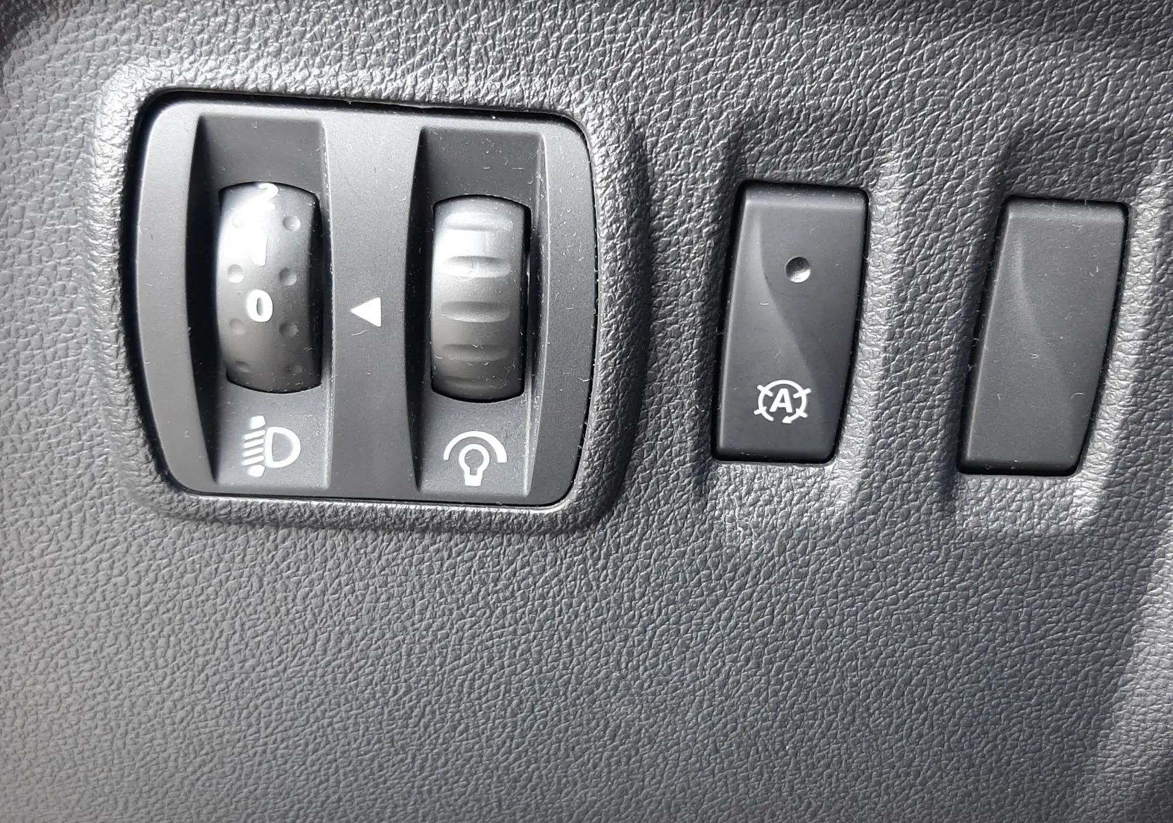 Gros plan sur les commandes de réglage des phares et de l'arrêt automatique du moteur d'un Renault Captur gris cassiopée toit noir.