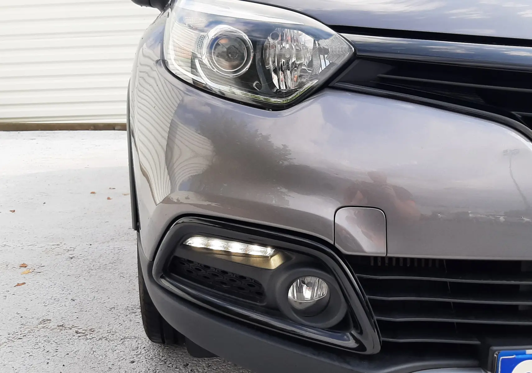 Gros plan sur l'avant gauche gris cassiopée du Renault Captur 2016, mettant en valeur le phare et le feu diurne LED.