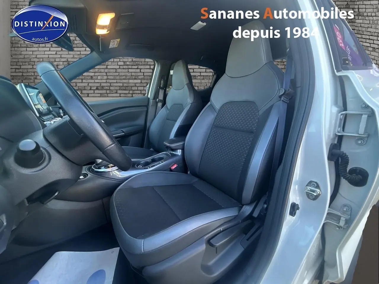Vue intérieure côté conducteur du Nissan Juke blanc 2024, montrant les sièges avant en tissu et cuir noir.