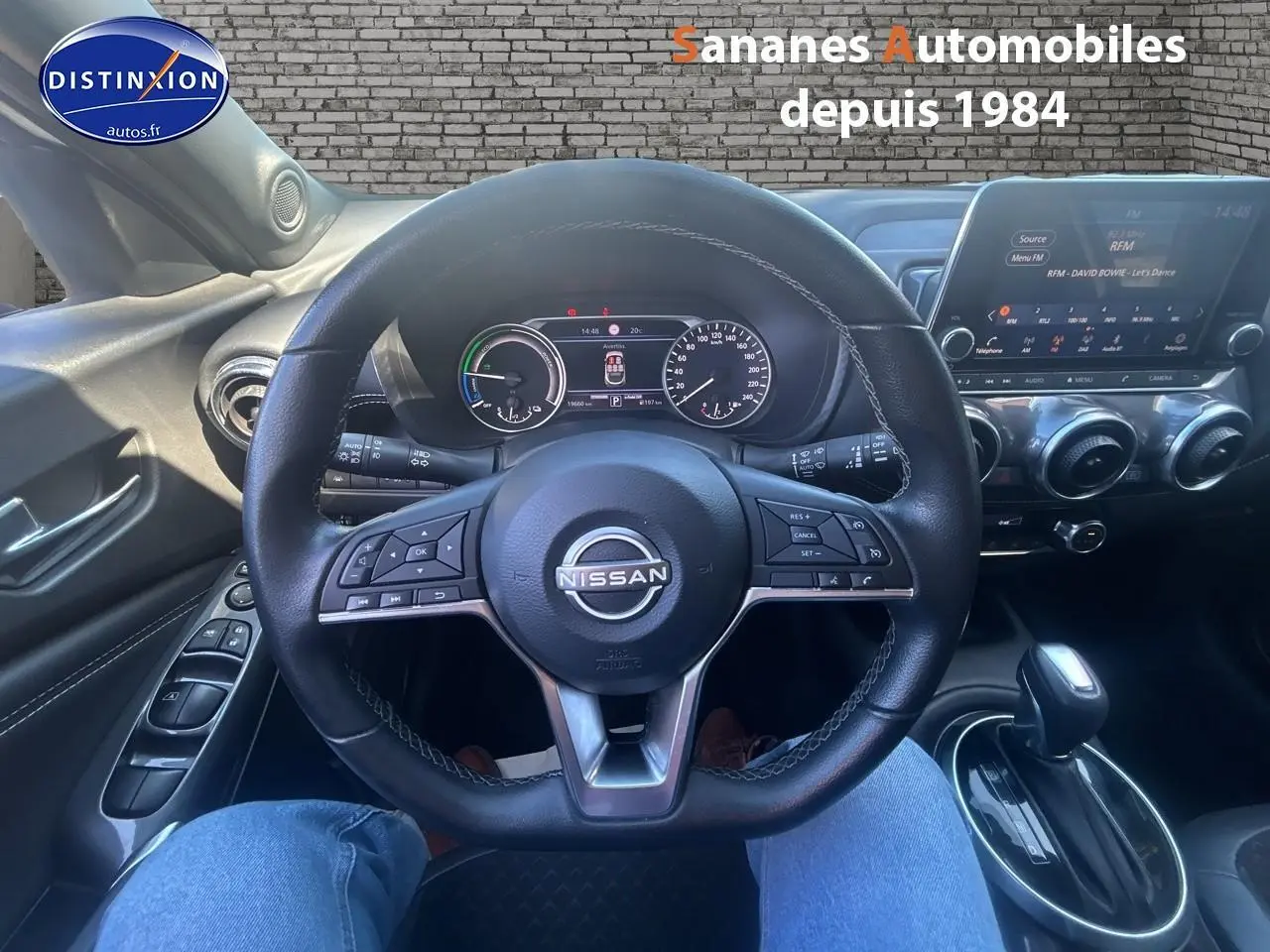 Vue intérieure centrée sur le volant et tableau de bord du Nissan Juke blanc 2024 avec écran tactile et commandes au volant.