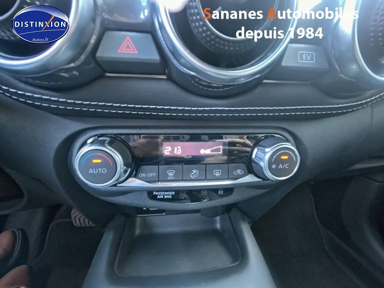 Vue rapprochée du tableau de bord du Nissan Juke blanc 2024, mettant en valeur la climatisation automatique et les commandes centrales.