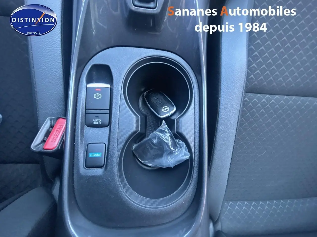 Gros plan sur la console centrale noire du Nissan Juke 2024 avec clé, bouton e-Pedal et frein à main électrique.