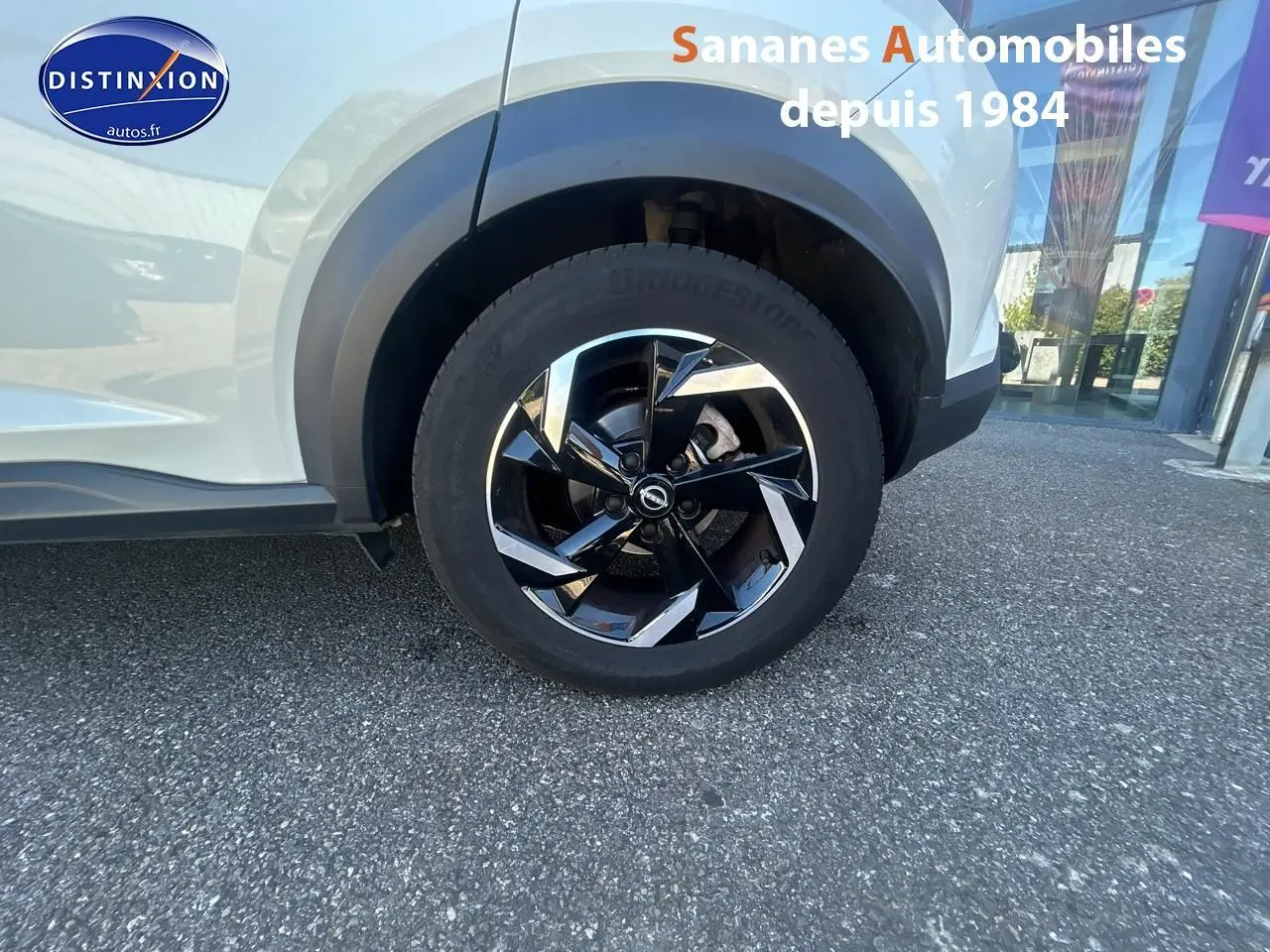 Gros plan sur la roue avant droite du Nissan Juke blanc 2024 avec jante alliage noire et chromée.