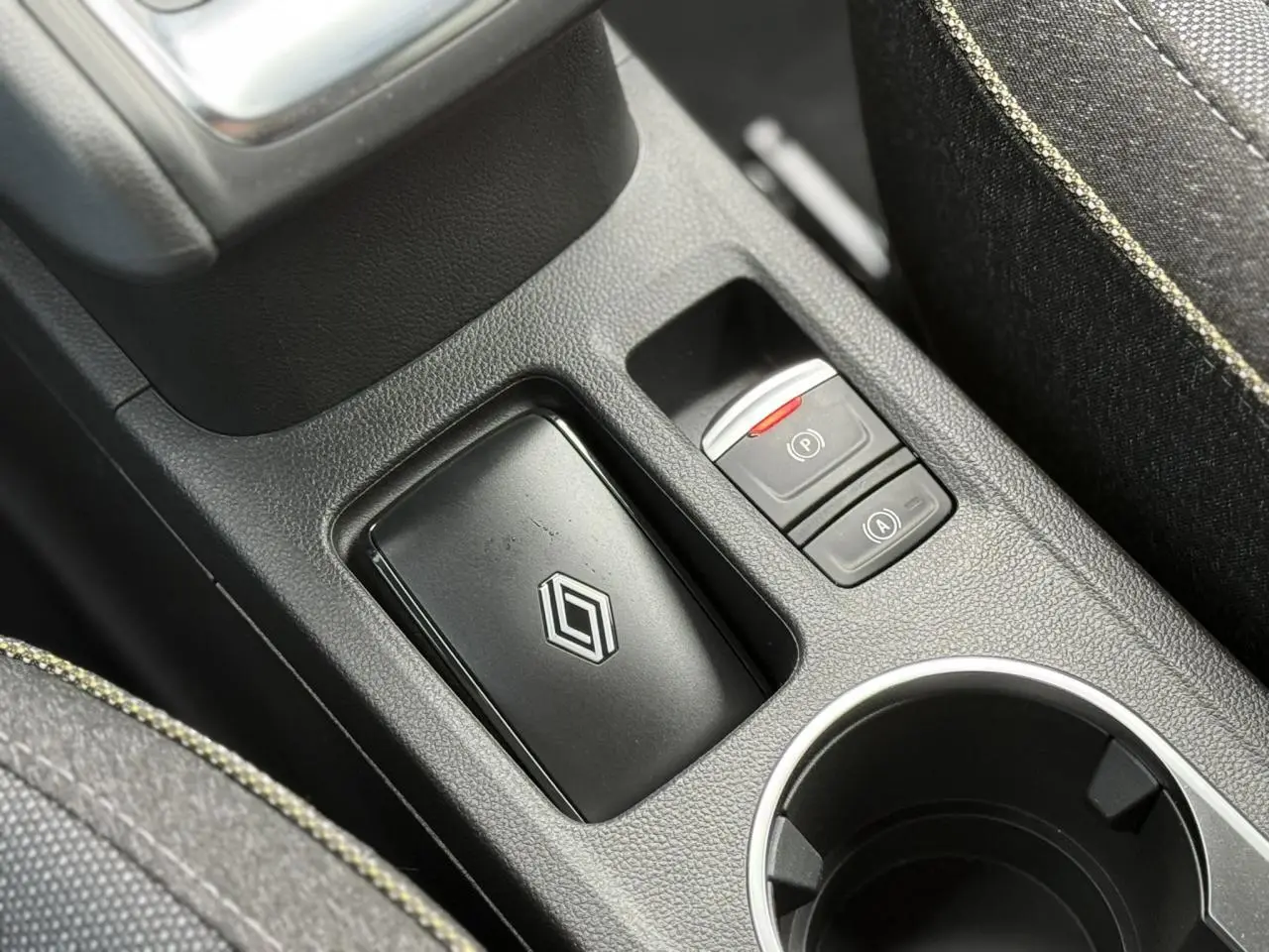 Gros plan sur la console centrale noire du Renault Captur blanc nacré, avec frein à main électrique et porte-clés Renault.