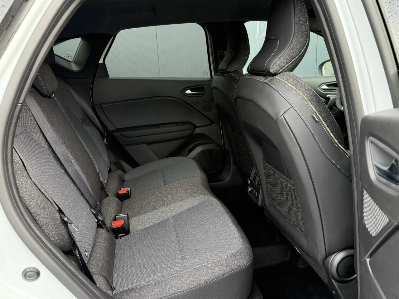 Vue intérieure côté gauche de la banquette arrière grise du Renault Captur 2025 avec sièges avant en cuir noir.