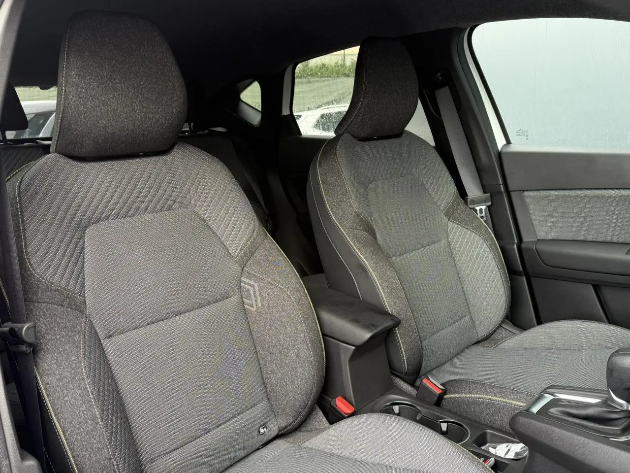 Vue intérieure des sièges avant gris foncé avec surpiqûres jaunes du Renault Captur hybride 2025, côté droit visible.