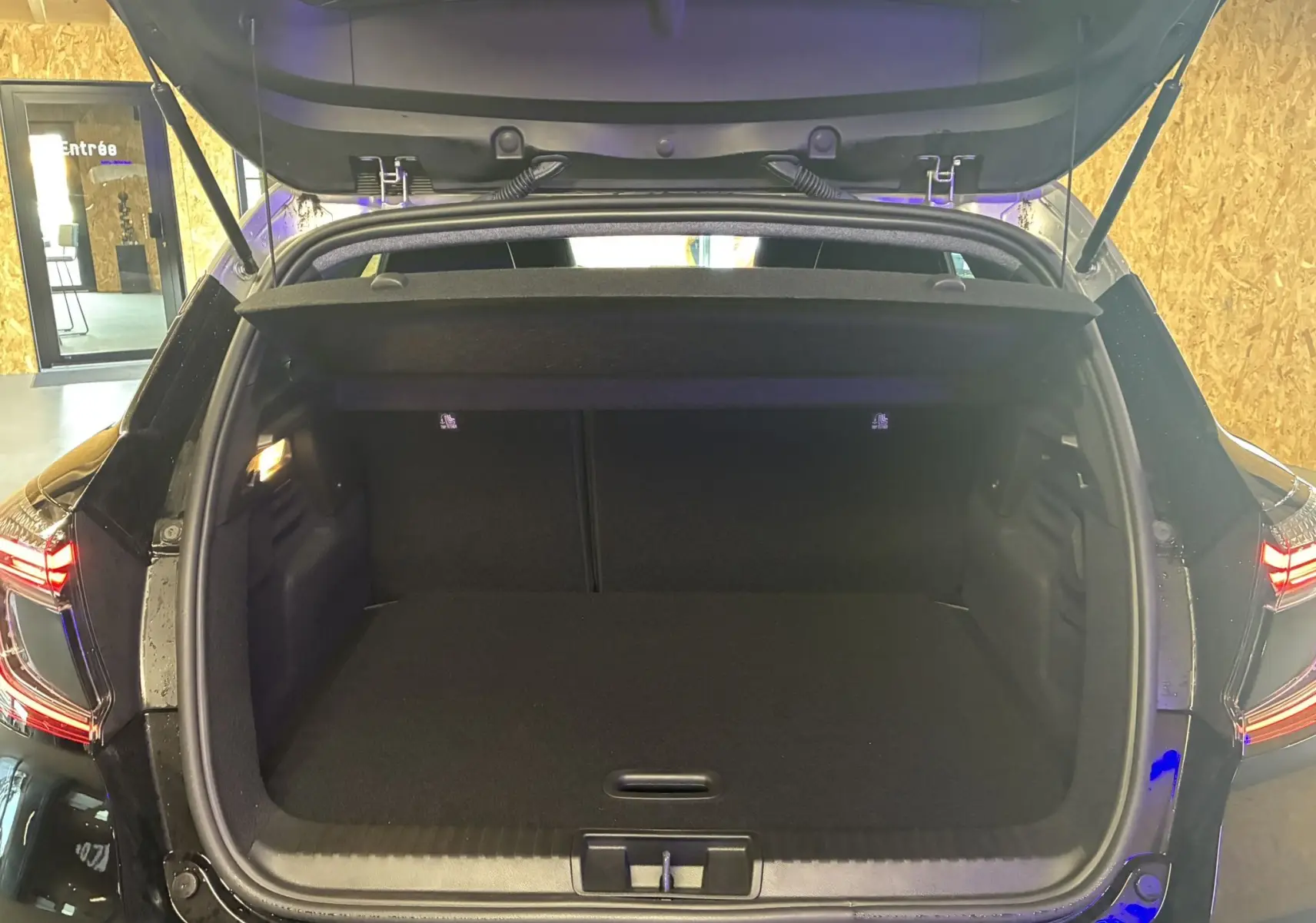 Coffre ouvert vu de l'arrière du Renault Captur noir étoile métal avec toit gris, intérieur spacieux et éclairage latéral.