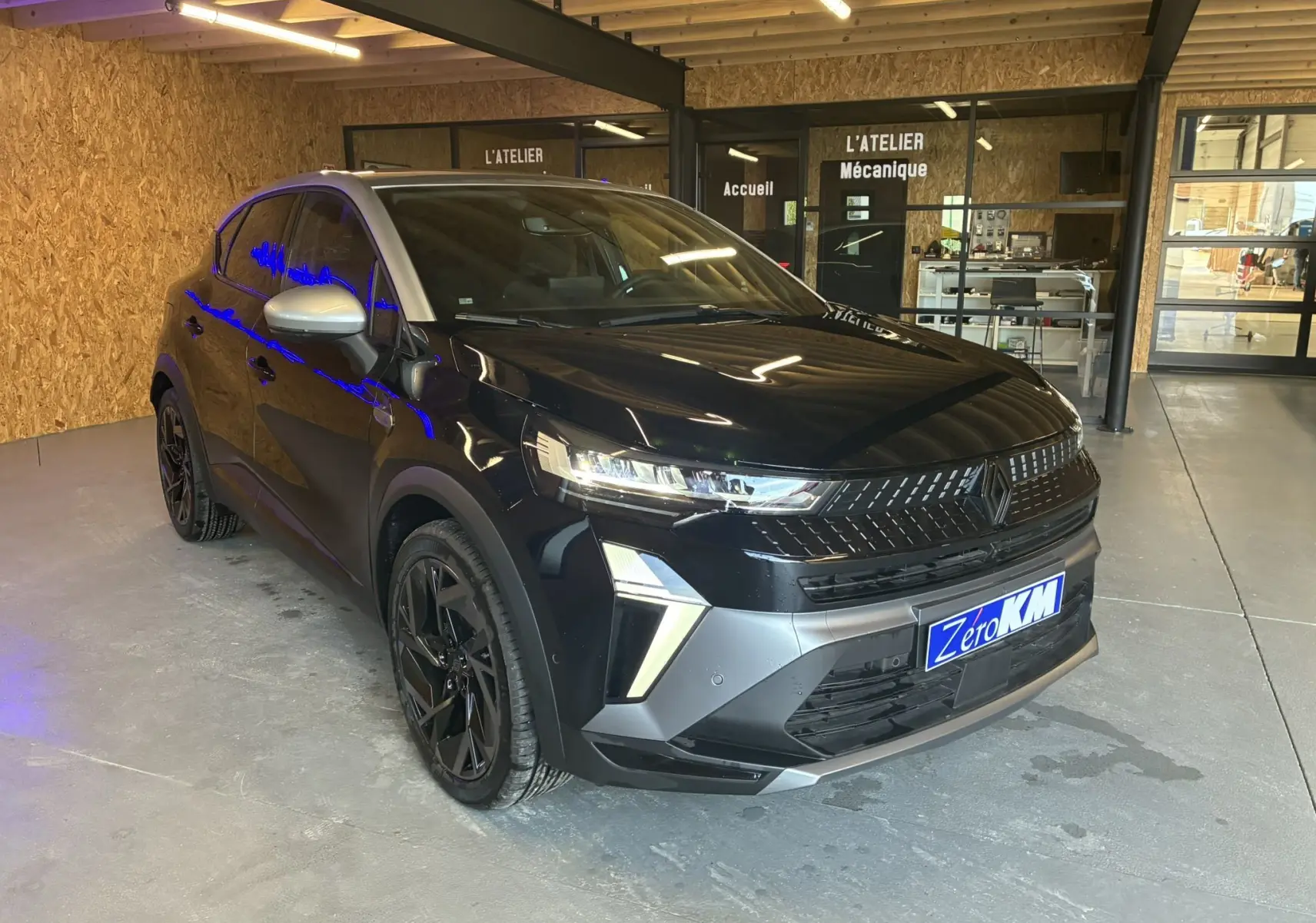 Renault Captur E-Tech hybride 2025 noir étoile avec toit gris, vue 3/4 avant en intérieur d'atelier mécanique.