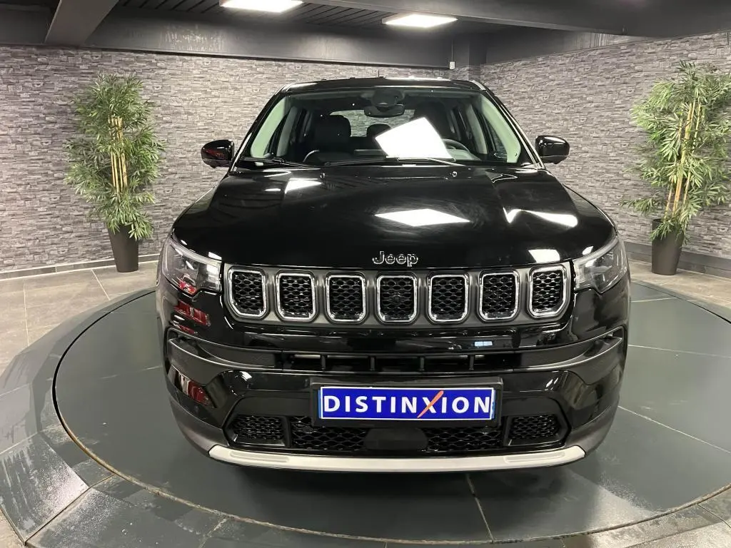 Vue frontale d'un Jeep Compass noir 2024 avec calandre chromée et plaque Distinxion dans un showroom.