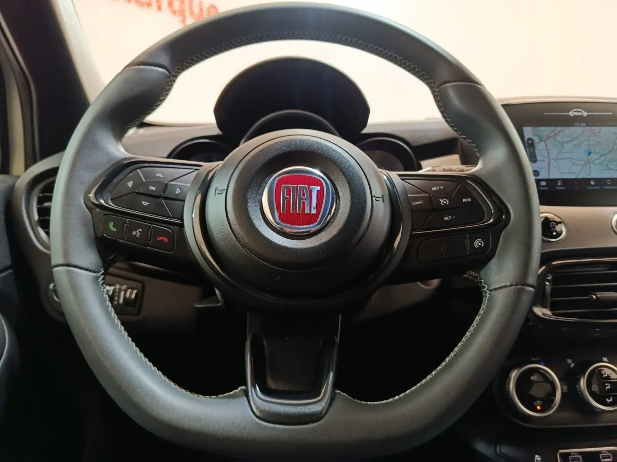 Vue rapprochée du volant noir de la Fiat 500X 2021 avec commandes intégrées et écran tactile de navigation visible.