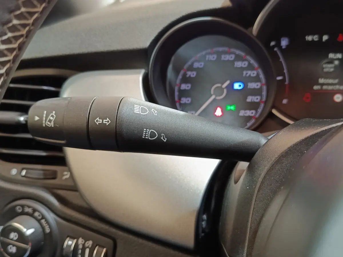 Gros plan sur la manette de clignotants noire du tableau de bord du Fiat 500X noir, avec compteur de vitesse en arrière-plan.