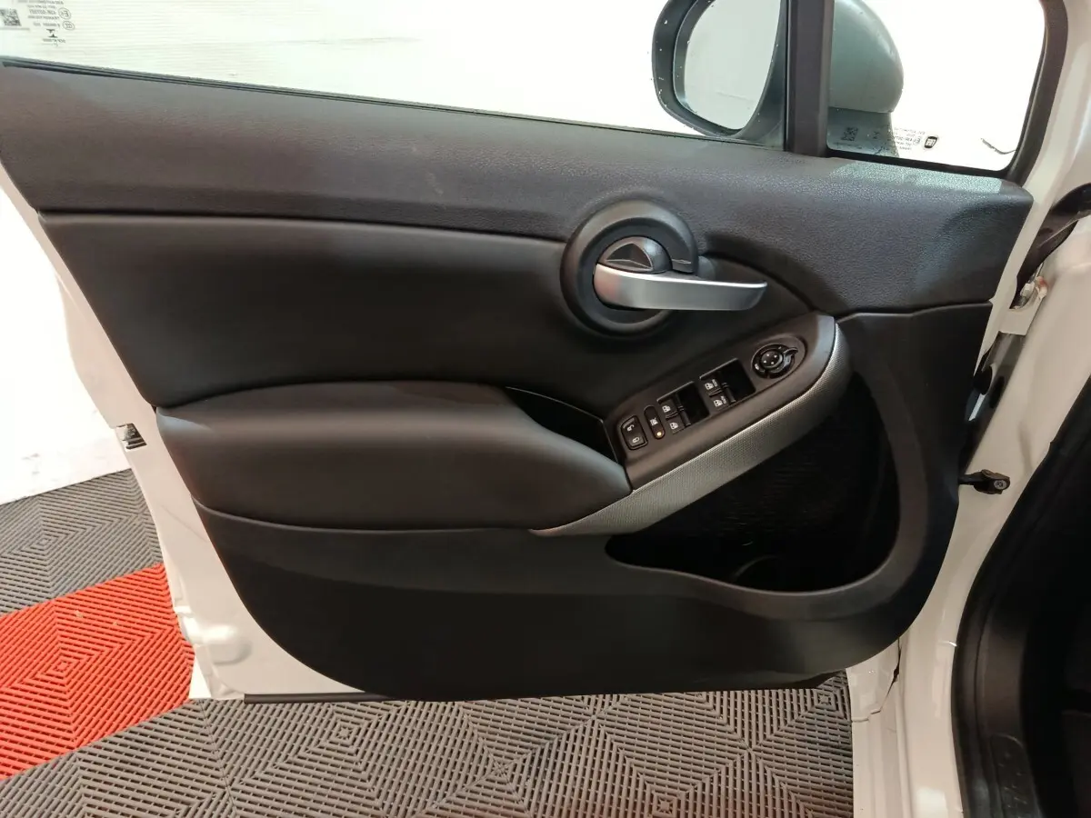 Vue intérieure côté gauche de la porte avant d'une FIAT 500X noire, avec commandes de vitres et poignée argentée.