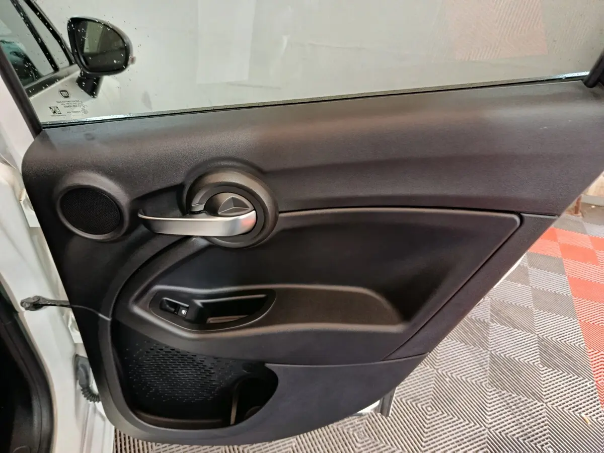 Vue intérieure de la porte arrière gauche noire du Fiat 500X, avec poignée argentée et commande de fenêtre.