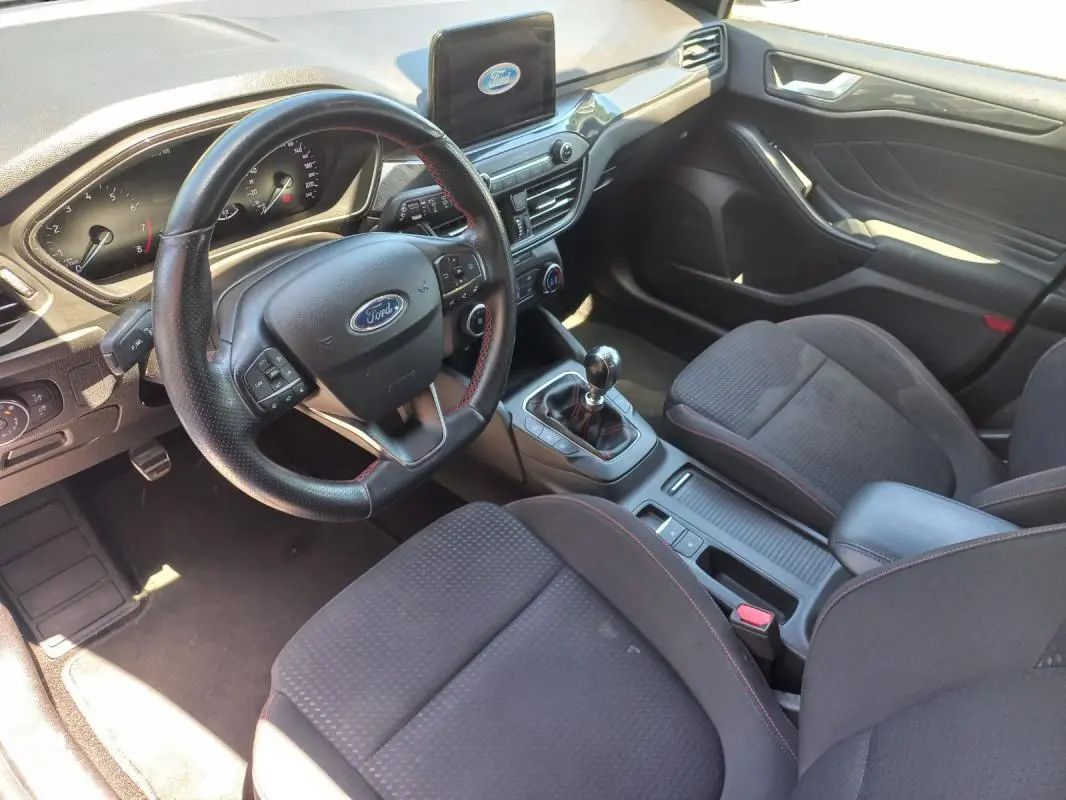 Vue intérieure côté conducteur de la Ford Focus 2019 avec volant cuir, écran central et levier de vitesse manuel.