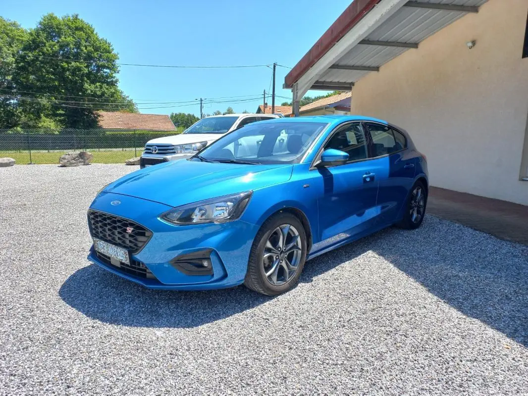 Ford Focus 1.0 SCTI ST-LINE bleu vue 3/4 avant droit, avec calandre noire et jantes alliage distinctives.