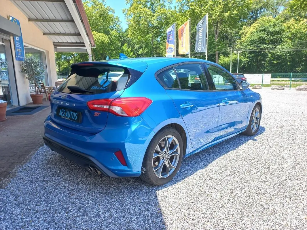 Vue 3/4 arrière droite d'une Ford Focus ST-Line bleu vif de 2019, avec jantes alliage et double sortie d'échappement.