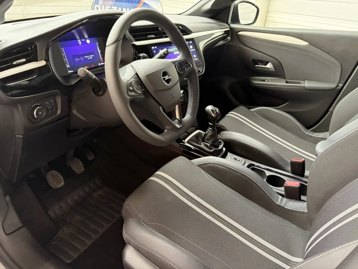Vue intérieure côté conducteur de l’Opel Corsa 2025, volant multifonctions cuir synthétique et sièges tissu gris à bandes claires.