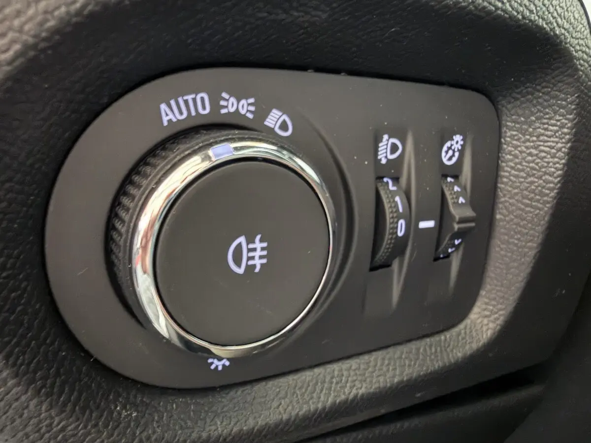 Gros plan sur la molette de réglage des phares d’un Opel Corsa gris clair, avec commandes d’éclairage et réglages associés.