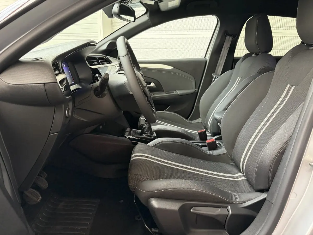 Vue intérieure côté conducteur de l'Opel Corsa 2025 gris clair, sièges noirs avec bandes blanches et volant multifonctions.