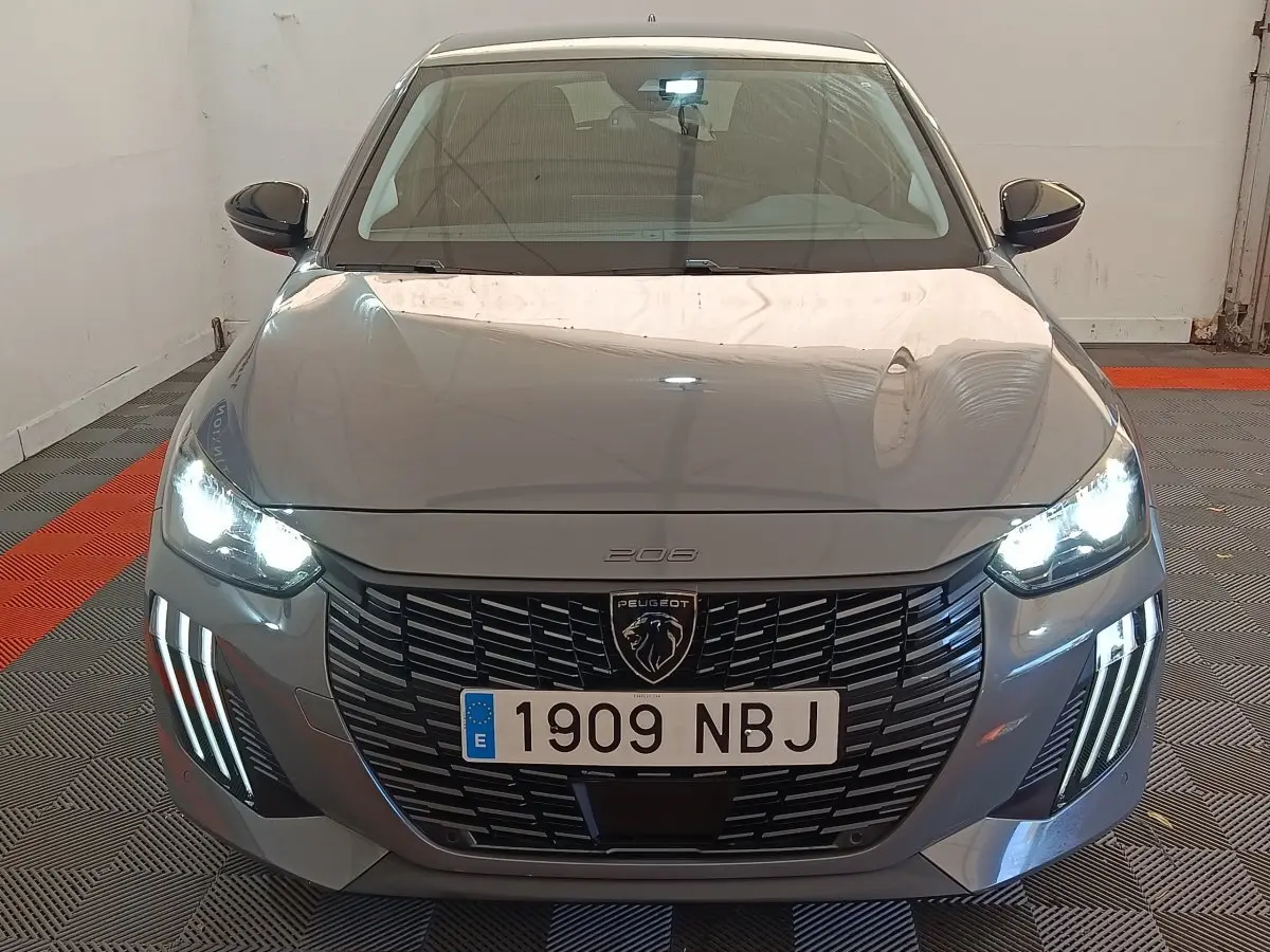Vue avant d'une Peugeot 208 PureTech 100 S&S Allure gris foncé avec phares LED allumés dans un garage.