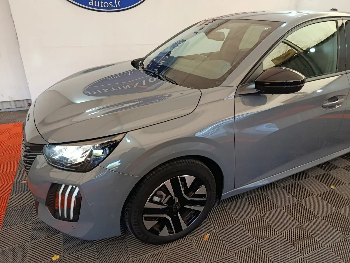 Vue 3/4 avant droit d'une Peugeot 208 gris foncé avec phares allumés et jantes noires distinctives.