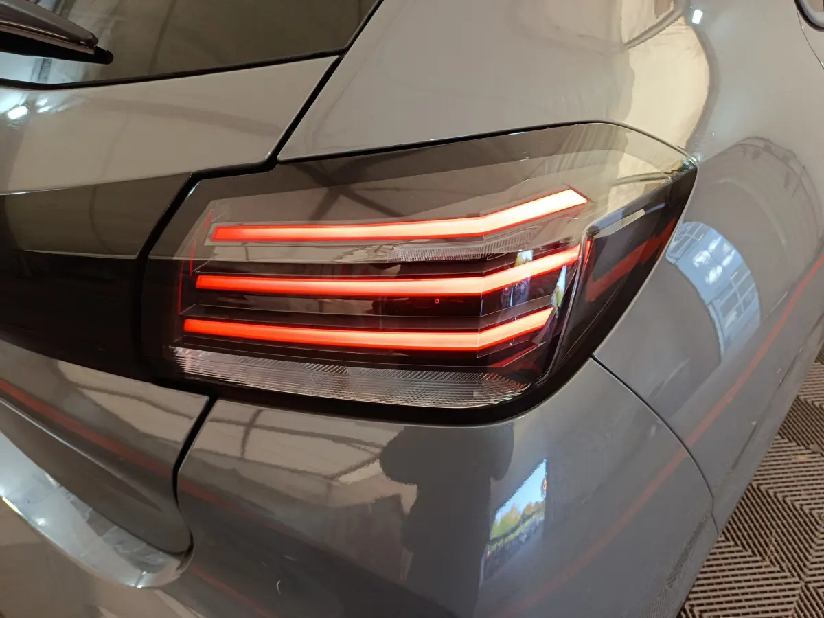 Gros plan sur le feu arrière droit allumé d'une Peugeot 208 gris foncé, mettant en valeur ses lignes LED distinctives.