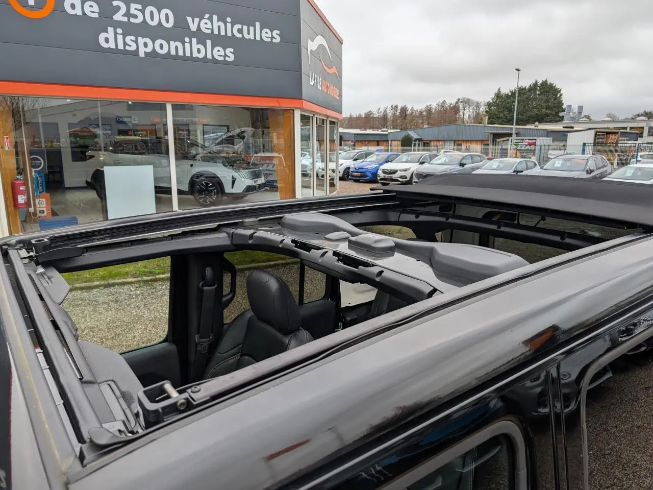 Vue rapprochée du toit panoramique ouvert d’un Jeep Wrangler noir, montrant l’intérieur et la structure du toit.