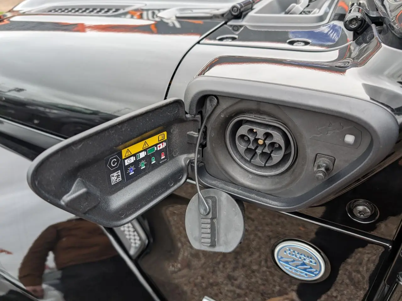 Détail de la prise de recharge hybride côté gauche d’un Jeep Wrangler noir avec port ouvert et instructions visibles.