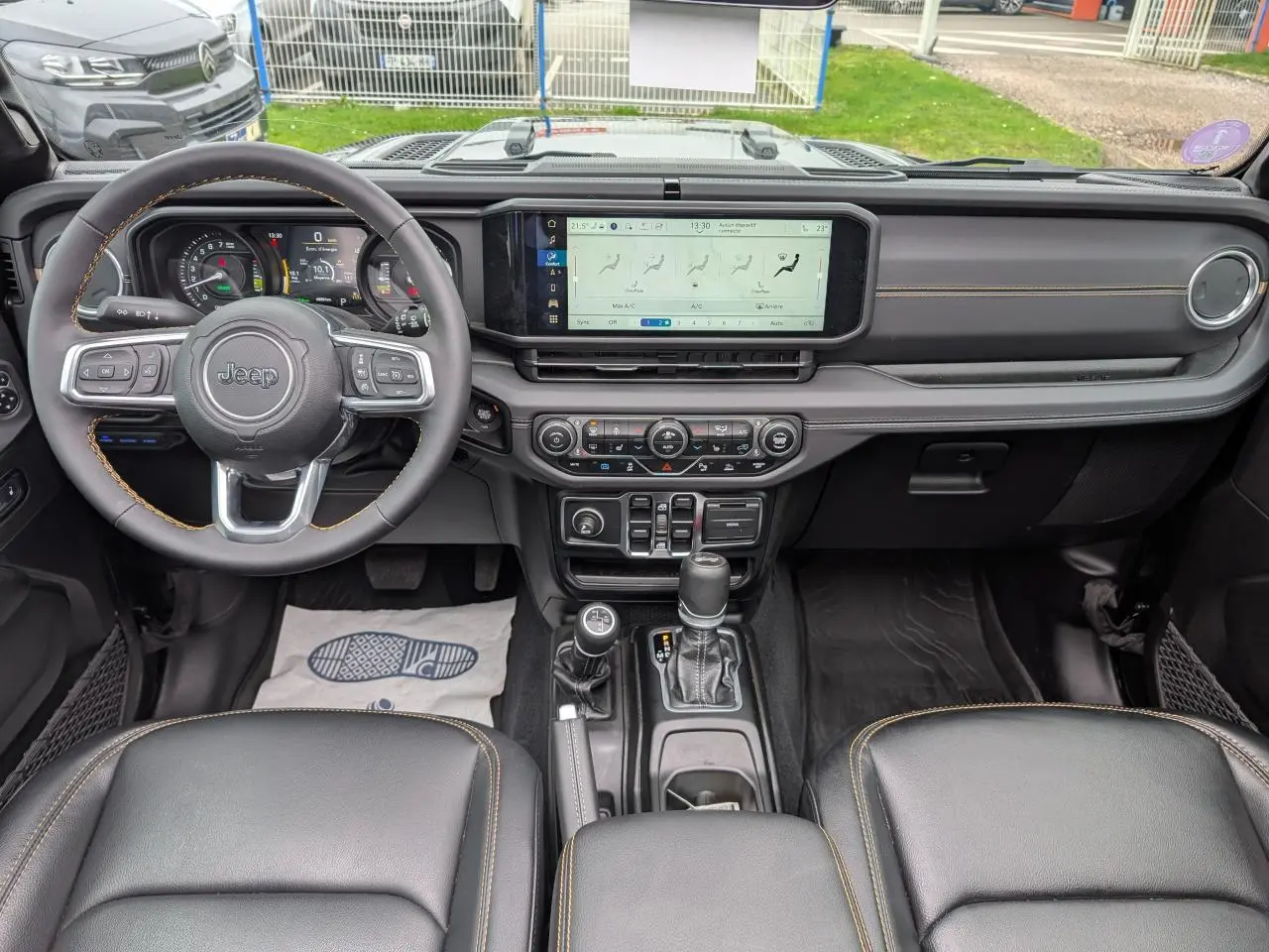 Vue intérieure avant du Jeep Wrangler 2024 noir, tableau de bord moderne avec écran tactile large et volant multifonctions.