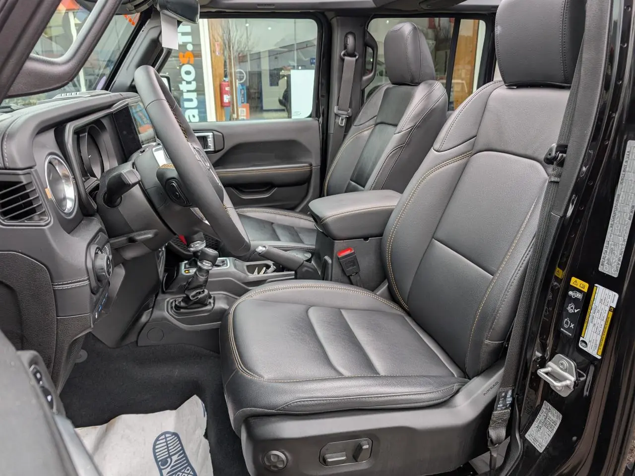 Vue intérieure côté gauche de la Jeep Wrangler 2024 noire, sièges TEP cuir noir avec surpiqûres jaunes visibles.