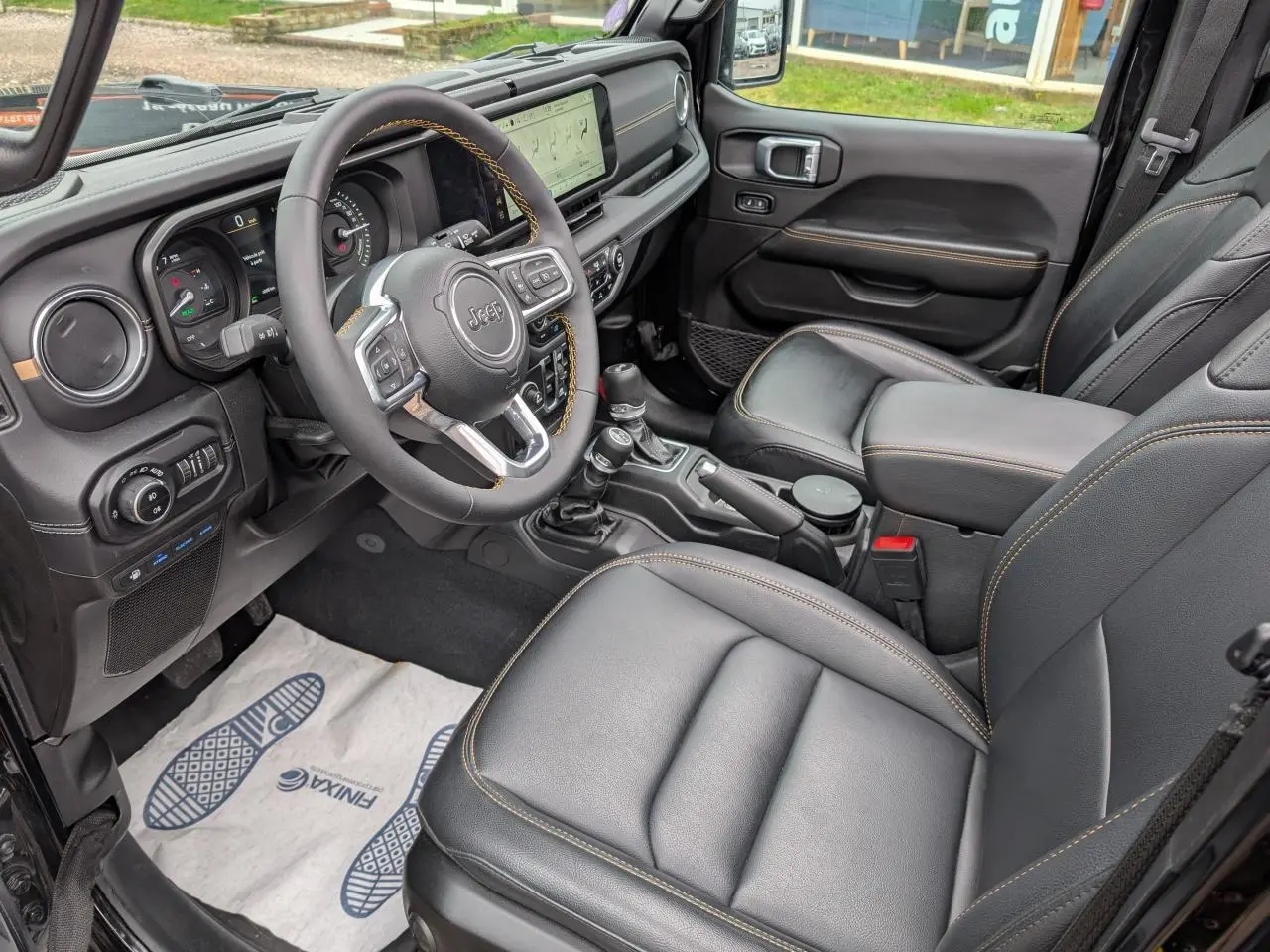 Vue intérieure côté conducteur de la Jeep Wrangler 2024, sellerie cuir noire avec surpiqûres jaunes et tableau de bord numérique.