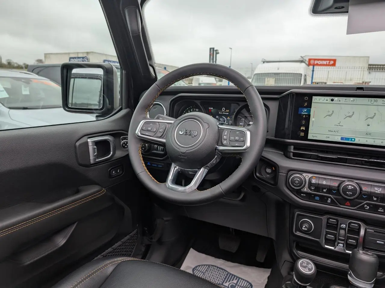 Vue intérieure côté conducteur du Jeep Wrangler 2024 noir, volant multifonctions avec surpiqûres jaunes et tableau de bord digital.