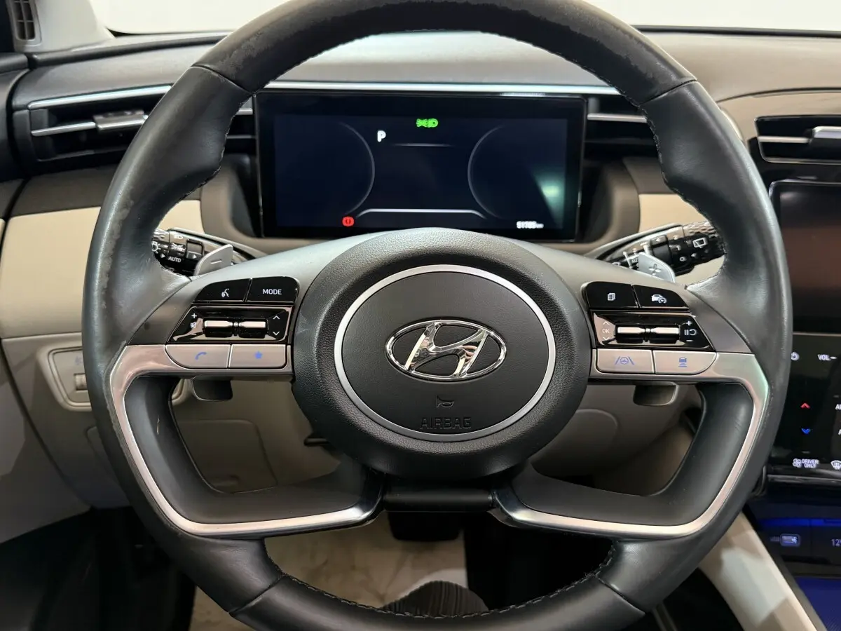 Vue rapprochée du volant cuir noir et alu du Hyundai Tucson 1.6 Hybrid 230 Executive avec tableau de bord numérique.