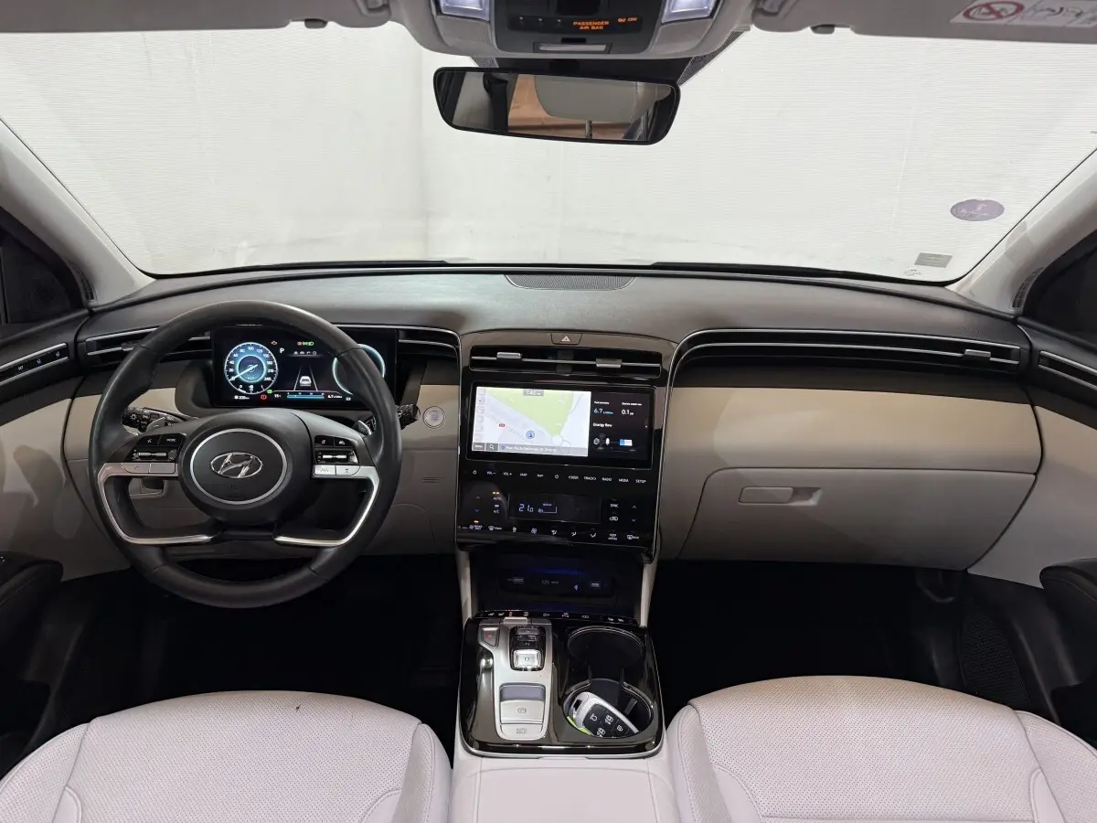 Vue intérieure avant du Hyundai Tucson 1.6 Hybrid 230 Executive avec tableau de bord beige et écran tactile central.