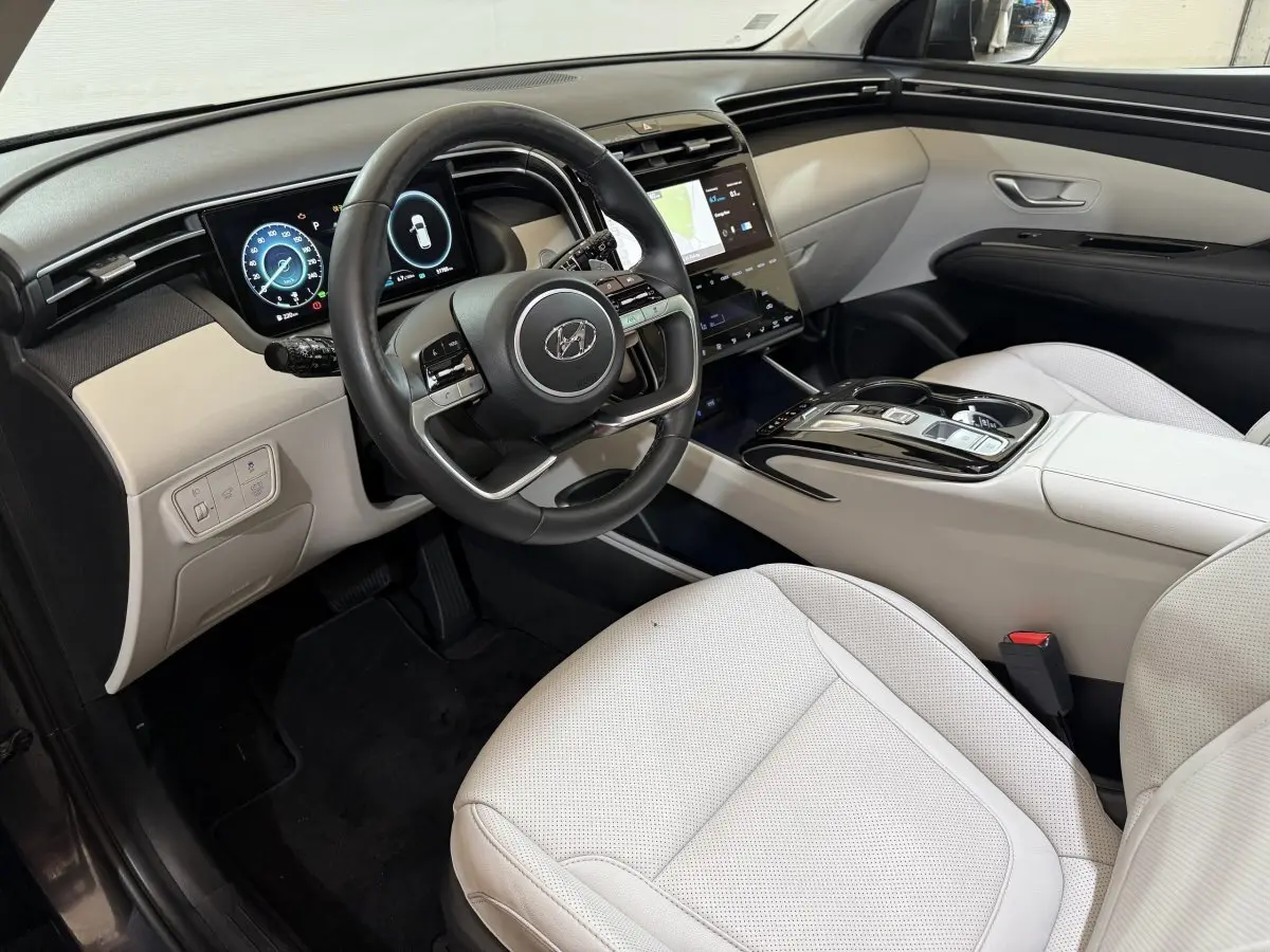 Vue intérieure côté conducteur du Hyundai Tucson 1.6 Hybrid 230 Executive avec sièges clairs et tableau de bord numérique.