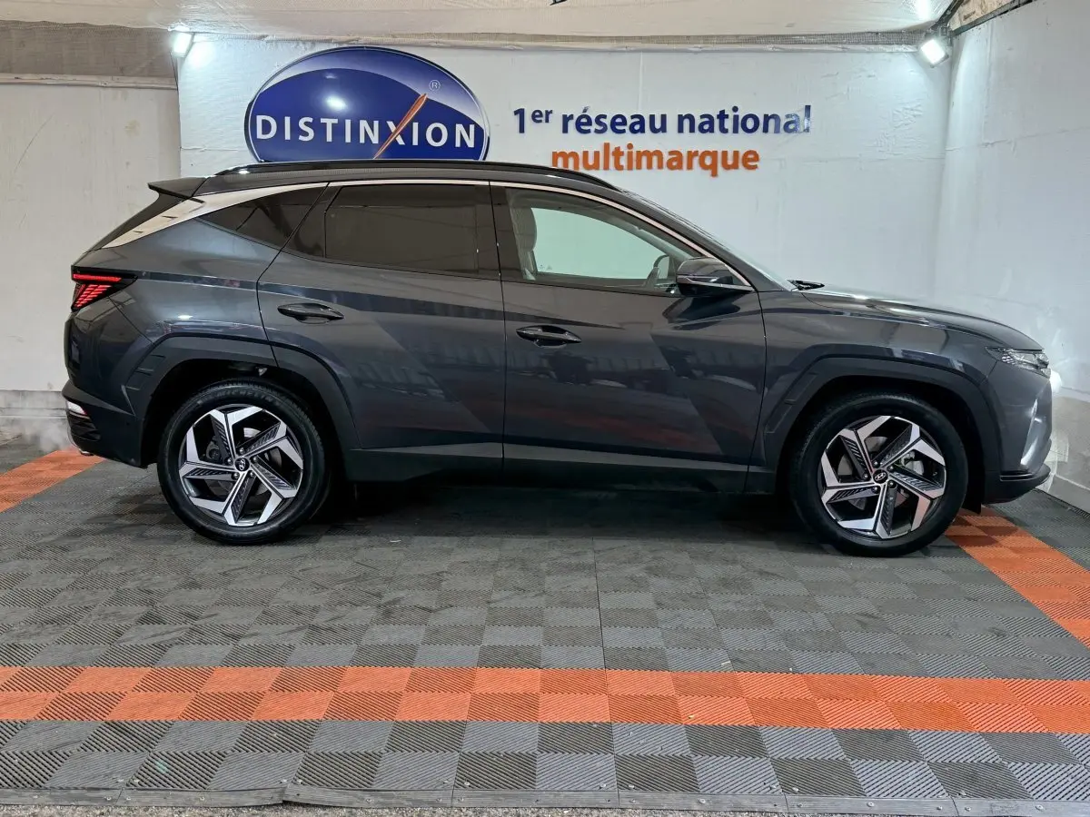 Vue de profil côté gauche d’un Hyundai Tucson gris foncé avec jantes alliage et vitres teintées en intérieur showroom.
