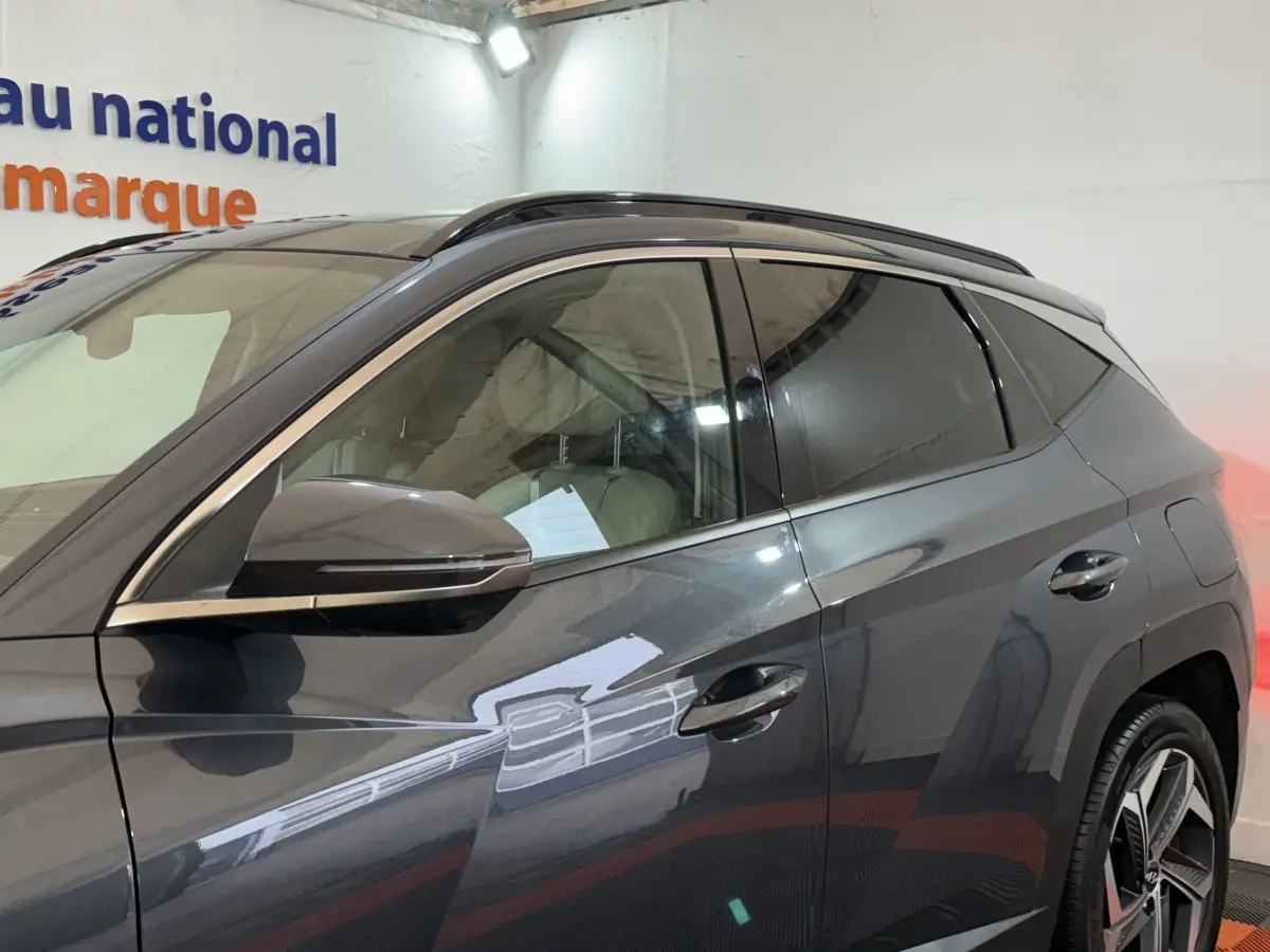 Vue de profil côté gauche du Hyundai Tucson gris foncé 1.6 Hybrid 230 Executive avec jantes alliage et barres de toit.