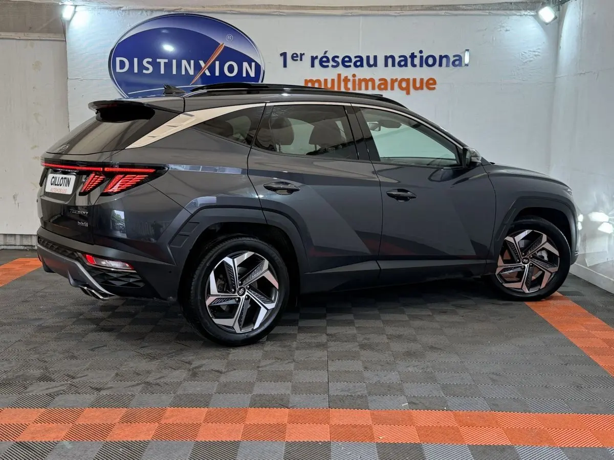 Vue latérale droite d'un Hyundai Tucson 1.6 Hybrid gris foncé avec jantes alliage et toit noir, en intérieur showroom.