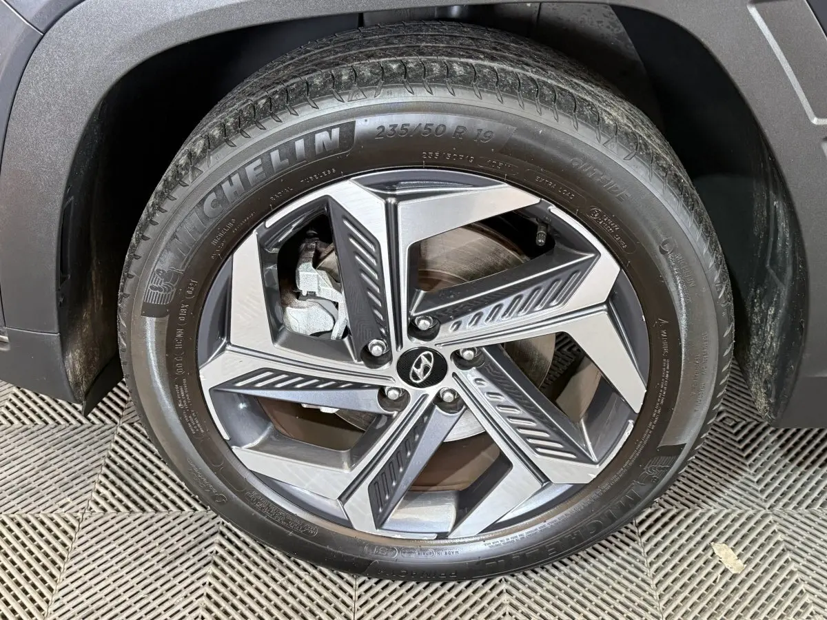 Gros plan sur la roue avant droite du Hyundai Tucson gris foncé, avec jante alliage au design géométrique moderne.
