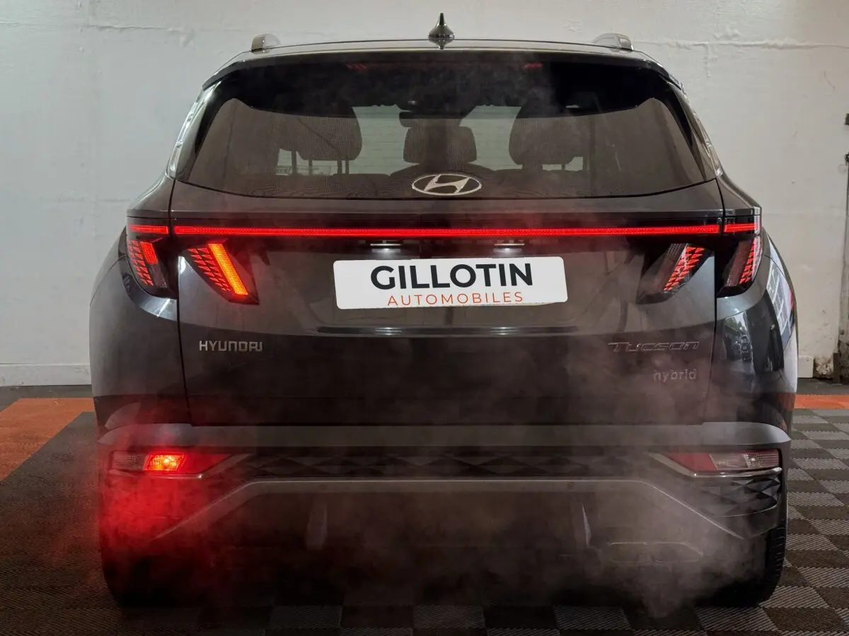 Vue arrière d'un Hyundai Tucson gris foncé avec feux arrière LED allumés et logo visible sur le hayon.